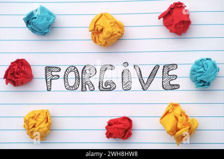 Forgive. The word Forgive written on a notebook sheet with some colorful crumpled paper balls around it. Close up. Stock Photo