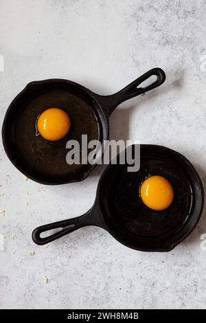 Two small cast iron frying pans with a raw egg in each one. Stock Photo