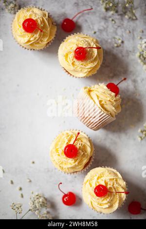 White chocolate cupcakes with piped white chocolate buttercream, grated white chocolate and maraschino cerries. Stock Photo