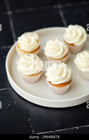 Mini vanilla cupcakes on a white plate and black tile background Stock Photo
