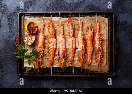 Grilled fried prawns shrimps Langostino Austral on skewers on metal grid baking sheet on black background Stock Photo