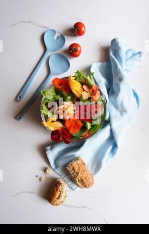 Mediterranean salad with zucchini, nasturtium, and rose edible flowers on white marble background flatlay. Stock Photo