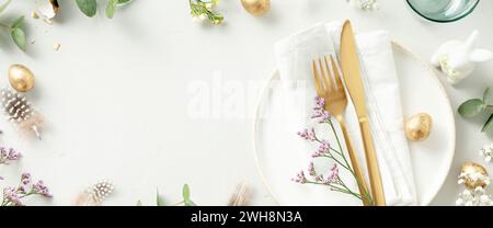 Easter table decorations. Stylish Easter brunch table setting with white plate, napkin, golden cutlery, easter eggs and spring branches on light grey Stock Photo