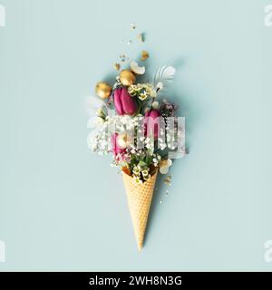Easter composition. Ice cream cone with beautiful flowers and golden easter eggs on blue background flat lay Stock Photo