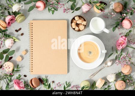 White cup of coffee, empty notebook and Frame made of Spring flowers and different types of macaroons flat lay mock up copy space Stock Photo