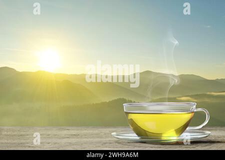 Aromatic green tea in glass cup on wooden table in mountains, space for text Stock Photo