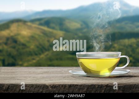 Aromatic green tea in glass cup on wooden table in mountains, space for text Stock Photo