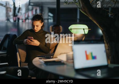 Happy millennial teen female checking social media holding smart phone at work. Stock Photo