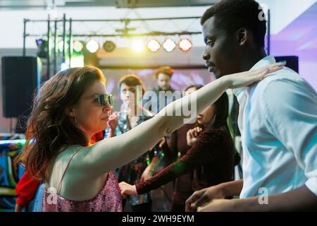 Young couple in love dancing while partying and relaxing in nightclub. Caucasian girlfriend and african american boyfriend making passionate moves on dancefloor while clubbing Stock Photo