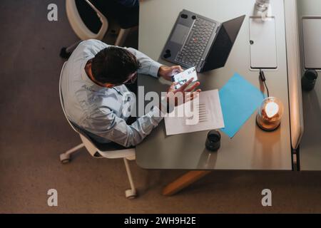 Professional senior man checking smart phone at modern workspace with laptop and documents. Stock Photo