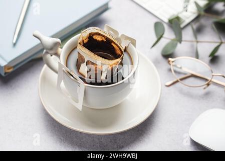 A glass cup of freshly brewed coffee with a handy drip coffee filter on office table.  Coffee break, quick way to brew hot drink Stock Photo
