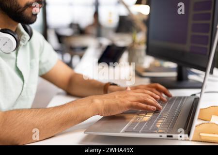 Young Asian man works on a laptop in a casual business office setting Stock Photo