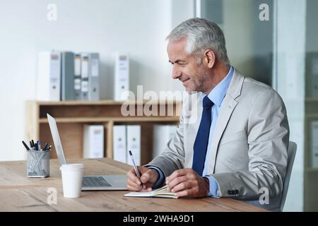 Man, boss and notes while working on laptop, coffee and office for stakeholder budget account. Senior, manager and indoors for company, book and Stock Photo