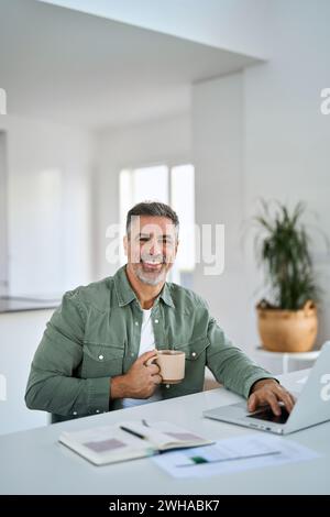 Happy older mature man drinking coffee using laptop at home table. Portrait. Stock Photo