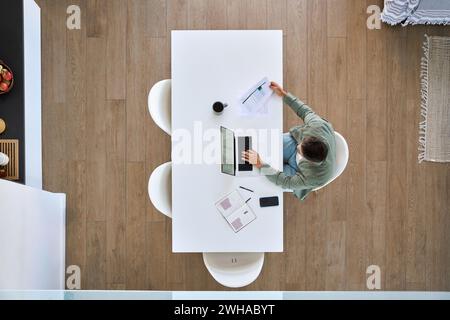 Mature man working on laptop sitting at kitchen home table, top view. Stock Photo