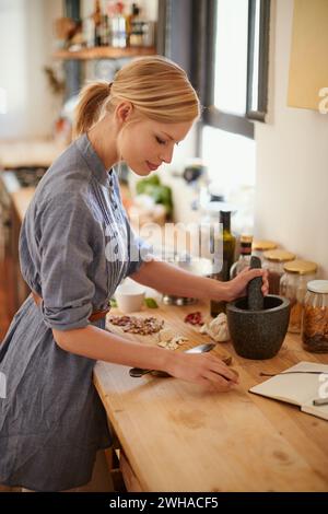 Cooking, woman and mortar with grind in a home with diet, nutrition and healthy food with pestle. Kitchen, bowl and happy from organic and vegan lunch Stock Photo