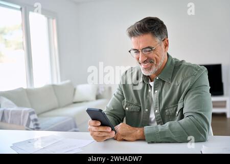 Happy older mature man using mobile cell phone at home in living room. Stock Photo