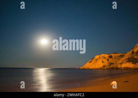 A serene coastal night illuminated by the full moon, casting a tranquil ...