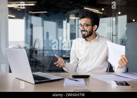 Smiling Indian businessman with beard, working at his desk in an office setting. Coding new software, exuding professionalism. Stock Photo