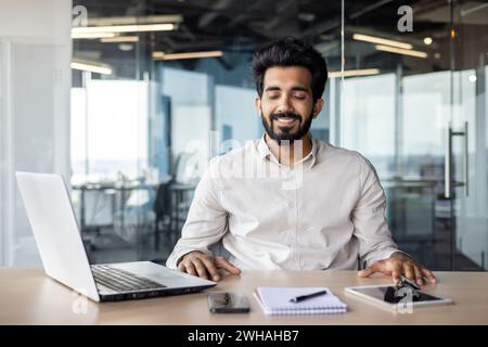 Indian businessman in a modern office working on a laptop with a cheerful disposition, portraying professionalism and focus. Stock Photo
