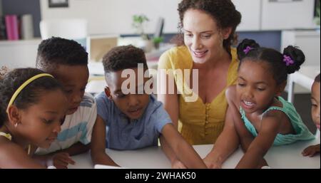 Image of school icons over happy diverse female teacher and pupils using laptop in class Stock Photo