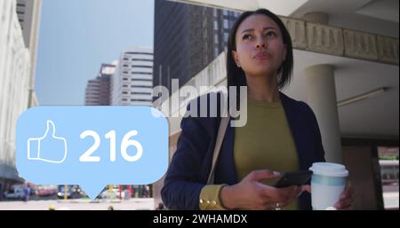 Image of like thumbs up icon with numbers changing over woman using smartphone in city Stock Photo