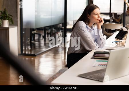 Young Caucasian woman sits thoughtfully at her casual business office desk Stock Photo