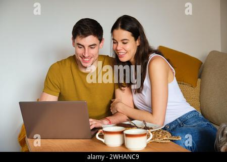 Happy couple using the laptop while having breakfast. Stock Photo