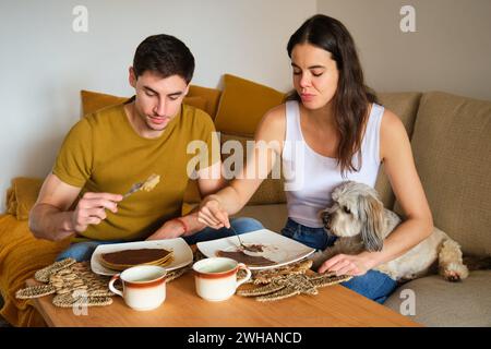 Spanish couple eating pancakes at home with their dog. Stock Photo