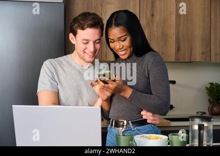 Multiracial happy couple using the phone at kitchen. Stock Photo