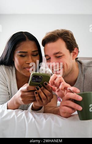 Multiethnic couple using the smartphone together on bed. Stock Photo