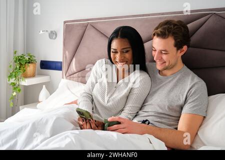 Multiracial couple laughing using the phone together on bed. Stock Photo