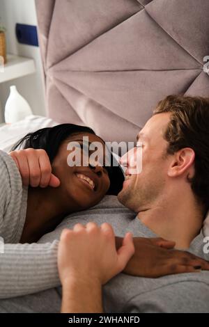 Multiethnic couple in love embracing and lying on bed. Stock Photo