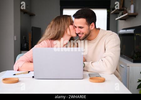 Woman kissing her boyfriend while using the laptop. Stock Photo