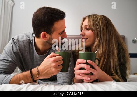 Spanish couple looking each other while drink coffee on bed. Stock Photo