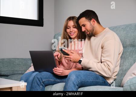 Spanish young couple using the phone and the laptop at home. Stock Photo