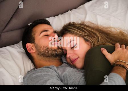 Spanish couple in love sleeping hugging on a bed. Stock Photo