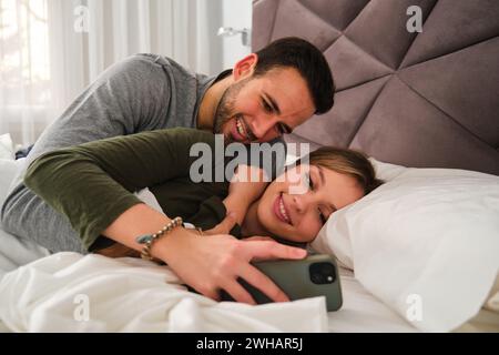 Spanish happy young couple using the phone together in bed. Stock Photo