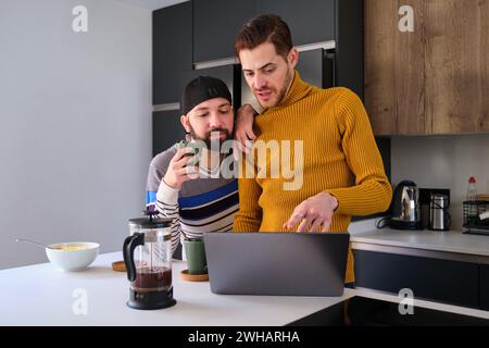 Homosexual couple using the laptop and talking while having breakfast. Stock Photo