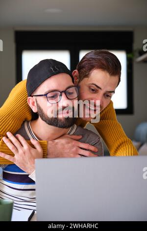 Homosexual couple using the laptop together hugging. Stock Photo