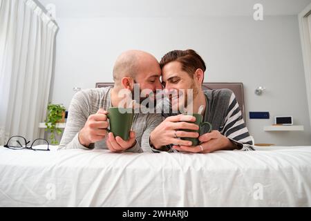 Homosexual couple in love drinking coffee in bed together. Stock Photo