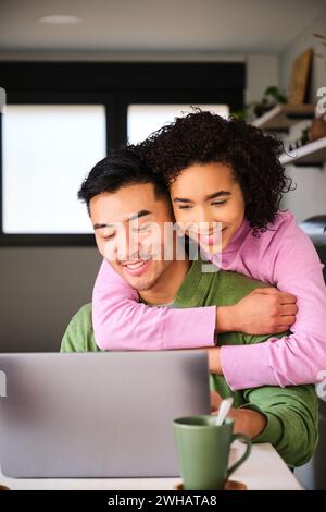 Multiracial happy couple using the laptop and hugging. Stock Photo