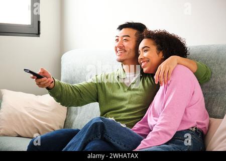 Multiethnic happy couple watching TV, movie or film together on sofa. Stock Photo
