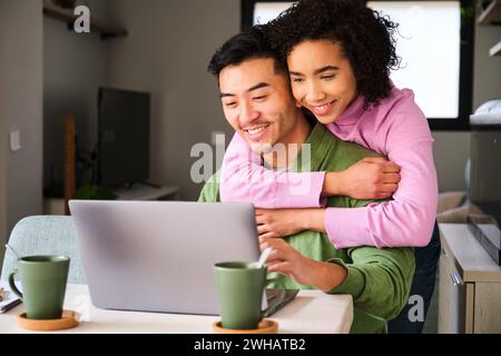 Multiethnic happy couple using the laptop and hugging. Stock Photo