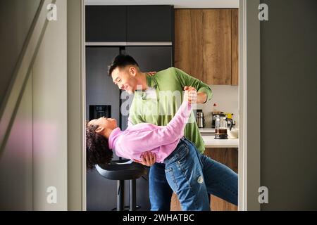 Multiethnic happy couple dancing in kitchen. Stock Photo