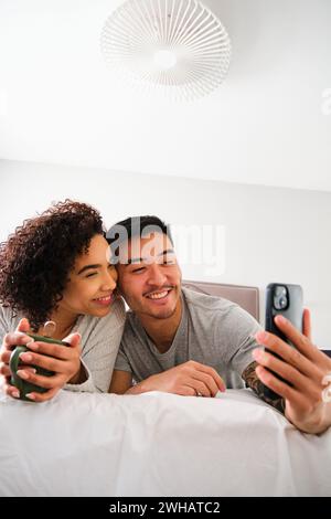Multiethnic happy couple taking a selfie on bed. Stock Photo