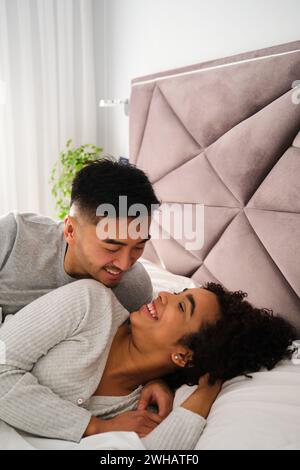 Multiethnic romantic couple wake up together in bed during honeymoon. Stock Photo