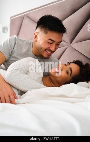 Multiracial romantic couple wake up together in bed during honeymoon. Stock Photo