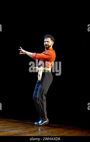 A male flamenco dancer with expressive hand gestures performs on stage, clad in a richly hued red shirt. Stock Photo