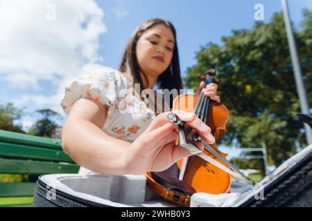 Closeup of hand of blurred latin woman outdoors sitting on wooden bench taking out violin bow from case to play in street. Stock Photo